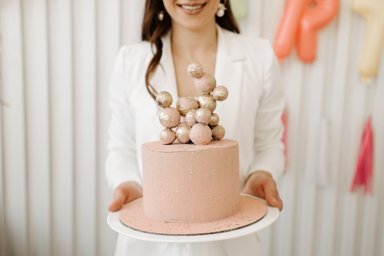 our-services-3 Pink cake with gold decorative balls held by woman in white blazer.