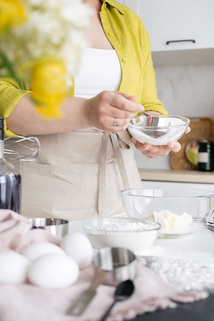 about-01 Crop unrecognizable female with measuring cup and icing sugar in bowl above cream during cooking process at home
